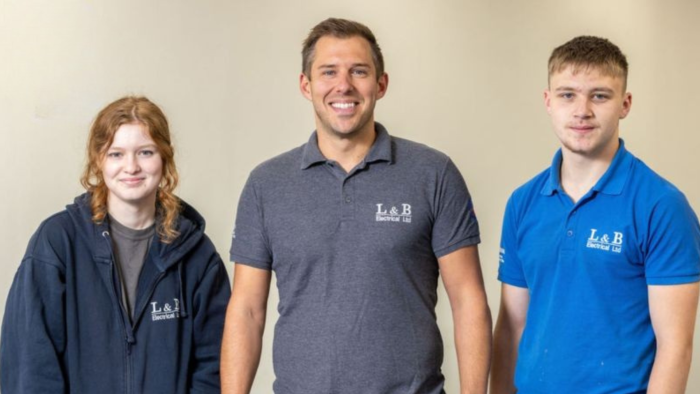 Three people wearing blue uniforms, two T Level students and their employer.