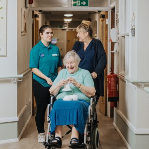 Student and care worker pushing an elderly woman in her wheelchair