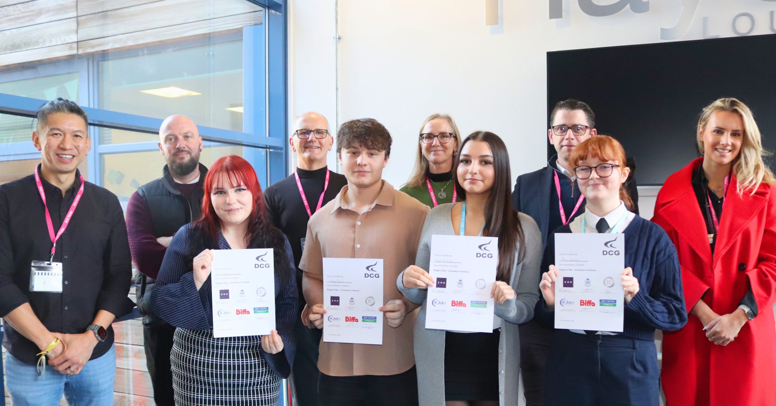 T Level ambassadors holding certificates in front of a display screen and signage, with others standing alongside them during a college T Level event.