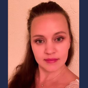 Person wearing a white top with lace detailing on one shoulder, standing against a light-coloured textured wall.