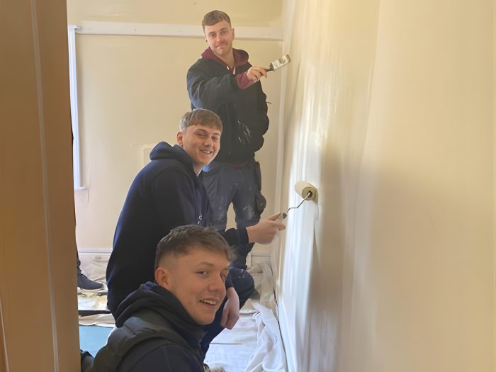 Apprentices painting and refurbishing the interior of a room as part of a hands‑on project supporting a children’s charity through real‑world apprenticeship experience.