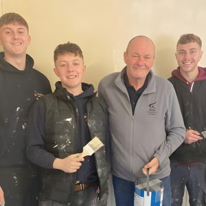 A group of apprentices holding paintbrushes and decorating materials while working together on a refurbishment project supporting a children’s charity.