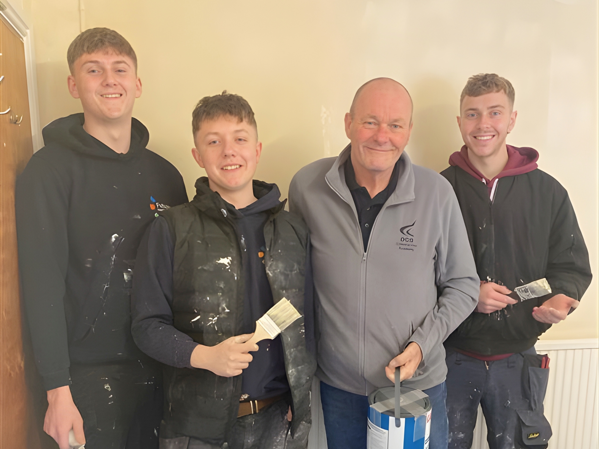 A group of apprentices holding paintbrushes and decorating materials while working together on a refurbishment project supporting a children’s charity.