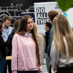 Students at a STEM and engineering event talk near industry exhibition stands, surrounded by engineering‑themed displays and informational banners.