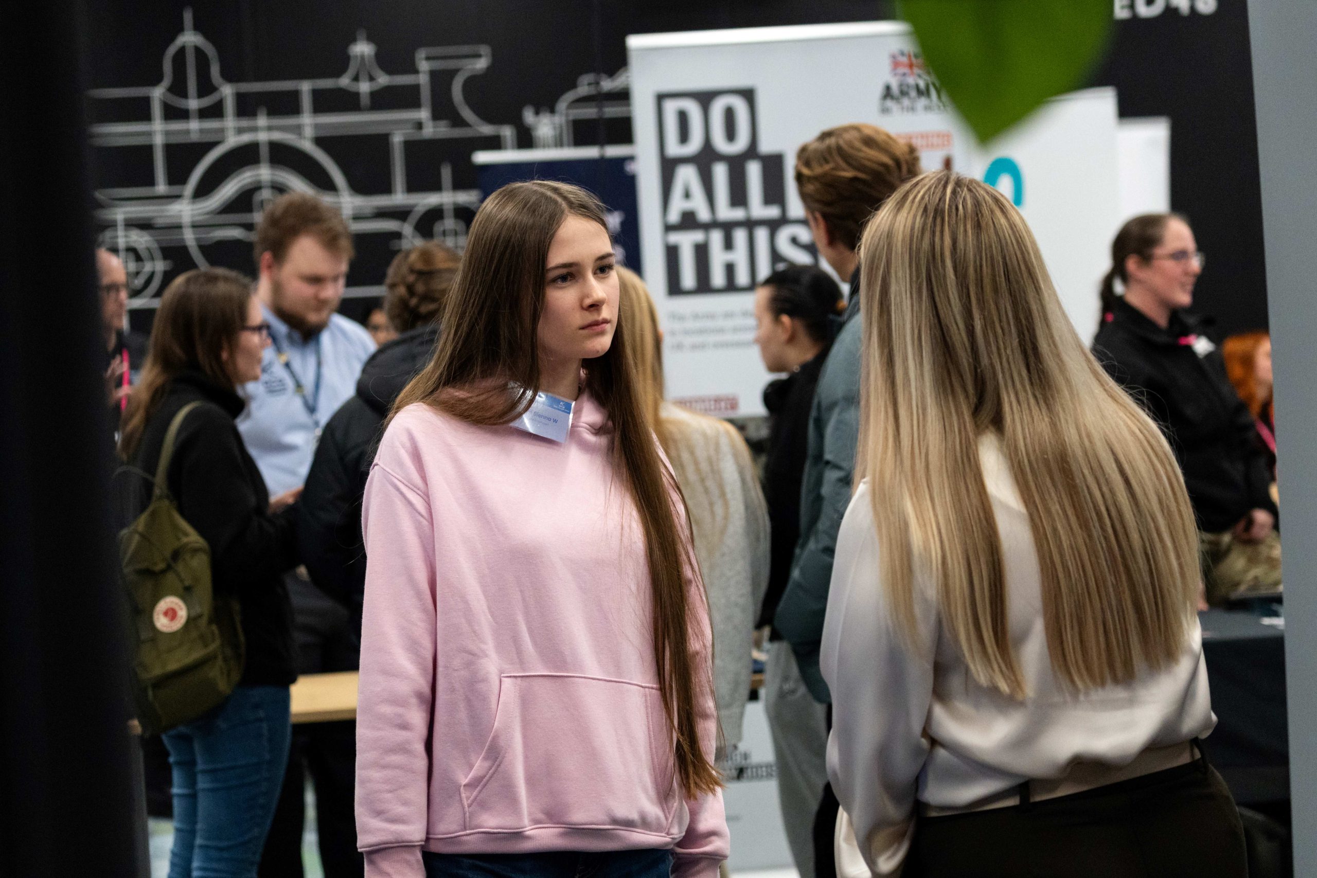 Students at a STEM and engineering event talk near industry exhibition stands, surrounded by engineering‑themed displays and informational banners.