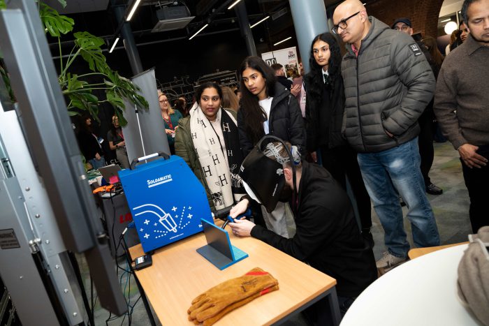 A crowd watches an engineering demonstration as an attendee uses welding equipment at a STEM event, showcasing hands‑on engineering skills and technology.