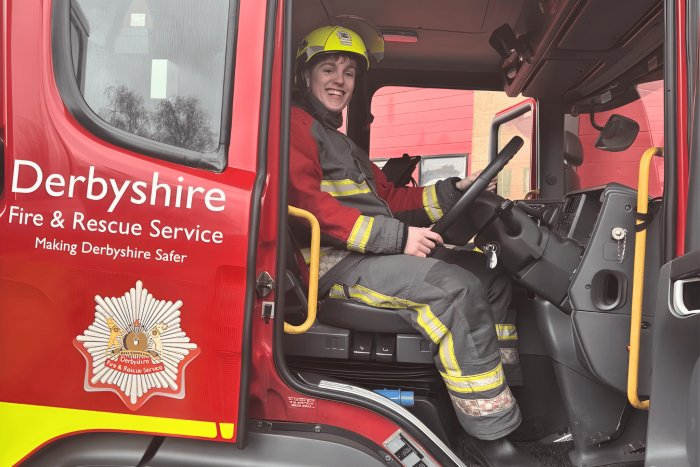 A Derby College student in full firefighter gear sitting inside a Derbyshire Fire & Rescue Service fire engine during a firefighter experience day.