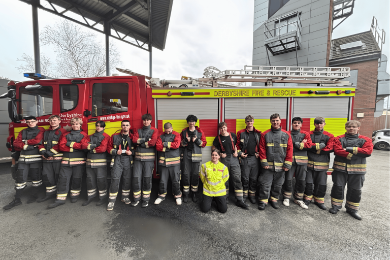 Derby College Public Services students standing in front of a Derbyshire Fire & Rescue Service fire engine during their firefighter experience day.