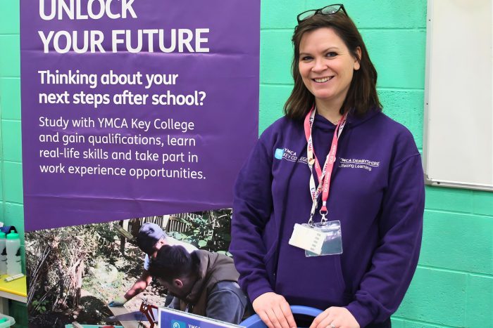 A YMCA Key College representative stands beside an information stand promoting study options, qualifications and work experience opportunities for young people at the Inclusion Showcase 2026.