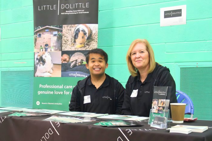 Little Dolittle exhibition stand with two representatives seated behind a table displaying brochures and promotional materials related to small animal care services.
