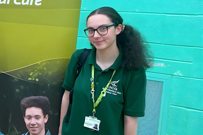 Student in a green DCG Animal Care uniform standing beside a Derby College Group banner at the Land‑Based Industry Insights event.