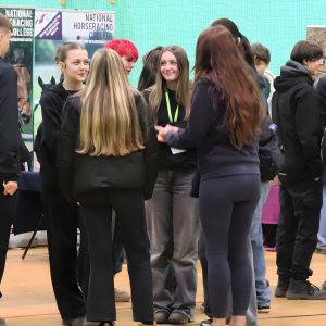 Group of students gathered in a sports hall, speaking with employers and exploring stands related to land‑based and animal care careers.