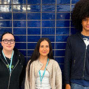 Three Derby College Group students who are young carers standing side by side in front of a blue tiled wall.