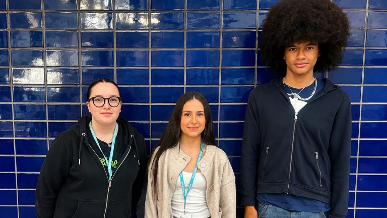 Three Derby College Group students who are young carers standing side by side in front of a blue tiled wall.