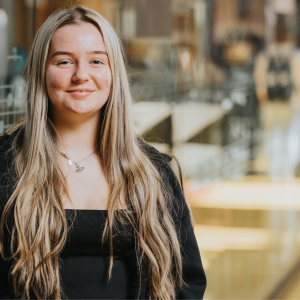 Derby College Group student Erin Lynott stood against a glass wall in a library.
