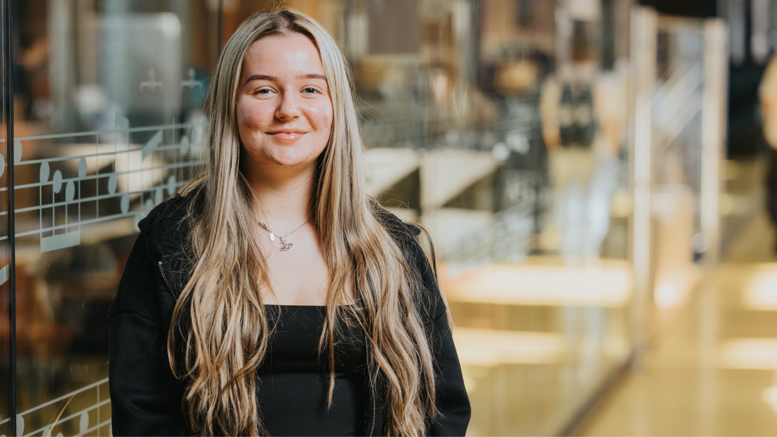 Derby College Group student Erin Lynott stood against a glass wall in a library.
