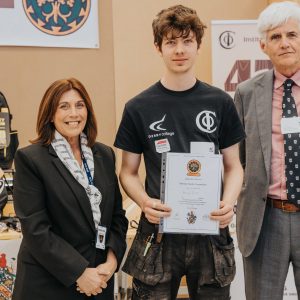 Derby College student holding an award with two more people who helped to organise the Marlene Trophy Competition.