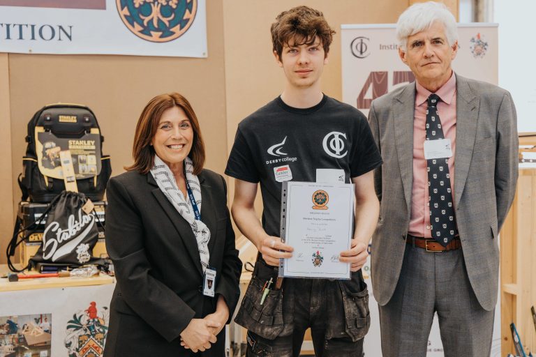 Derby College student holding an award with two more people who helped to organise the Marlene Trophy Competition.