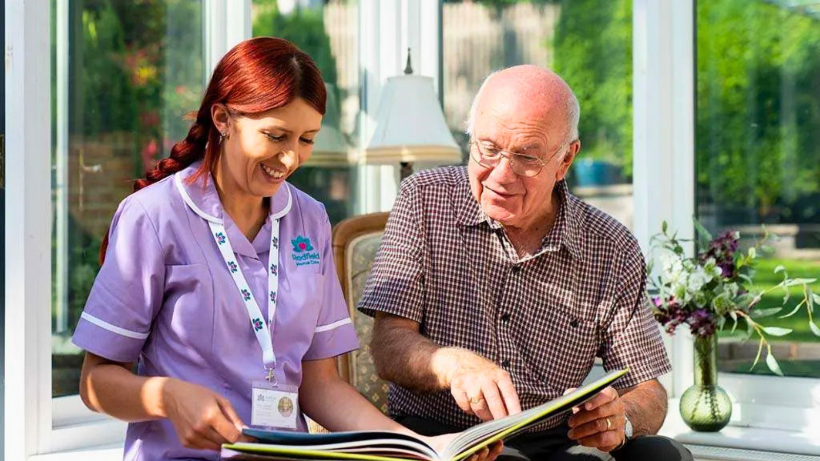 Elderly person reading a book with a carer from Radfield Home Care
