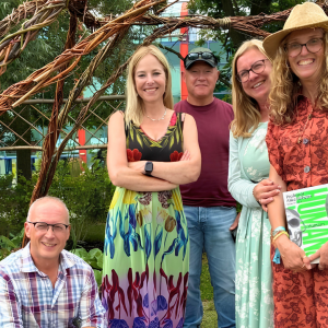 Five Derby College Horticulture students posing together in a garden, standing and crouching beneath a woven willow arch, with greenery and plants surrounding a mosaic feature on the ground in a landscaped outdoor creative space that won silver at Gardner's World Live