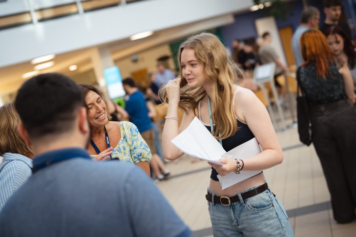 A-level student Ellie Middleton holding her results paper and smiling.