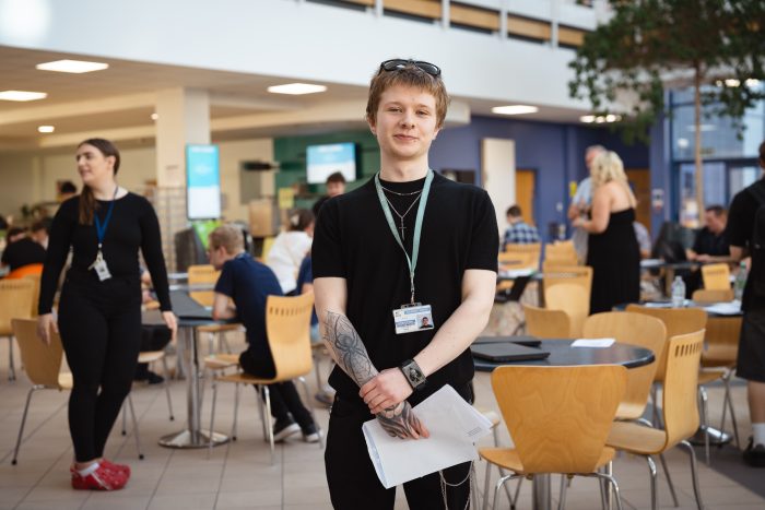 A-level student Kingsley Pickering wearing a black shirt holding a paper with his results on.
