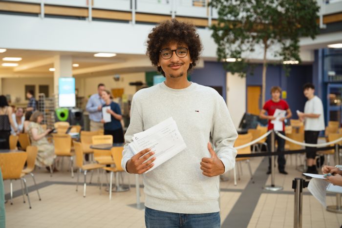 A-level student Oliver Roberts holding a paper with his results on and giving a thumbs up.