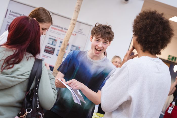Young people holding pieces of paper with their Level 3 results on them.