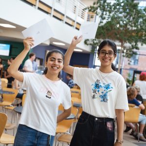 Derby College T Level students Lakshika Aarya and Mysha Fatima holding their results in the air.