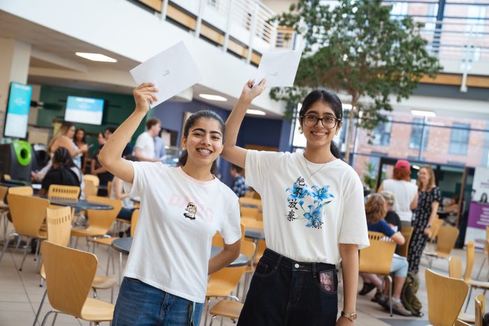 Derby College T Level students Lakshika Aarya and Mysha Fatima holding their results in the air.