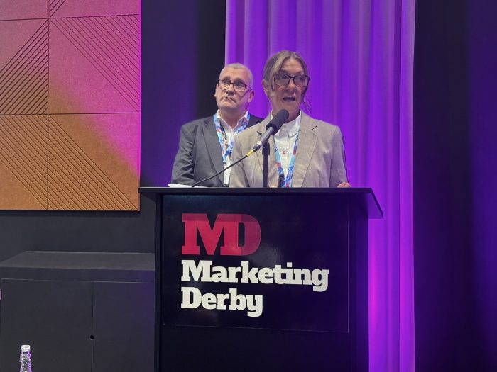 A speaker at the Derby Property Summit stood on a podium with another speaker behind them.