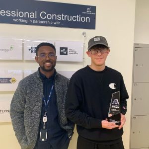 Teacher of CAD and BIM at Derby College, Eugene Gbenedio, wearing a blue shirt and grey jumper stood next to Derby College apprentice Daniel Burgin, holding his award