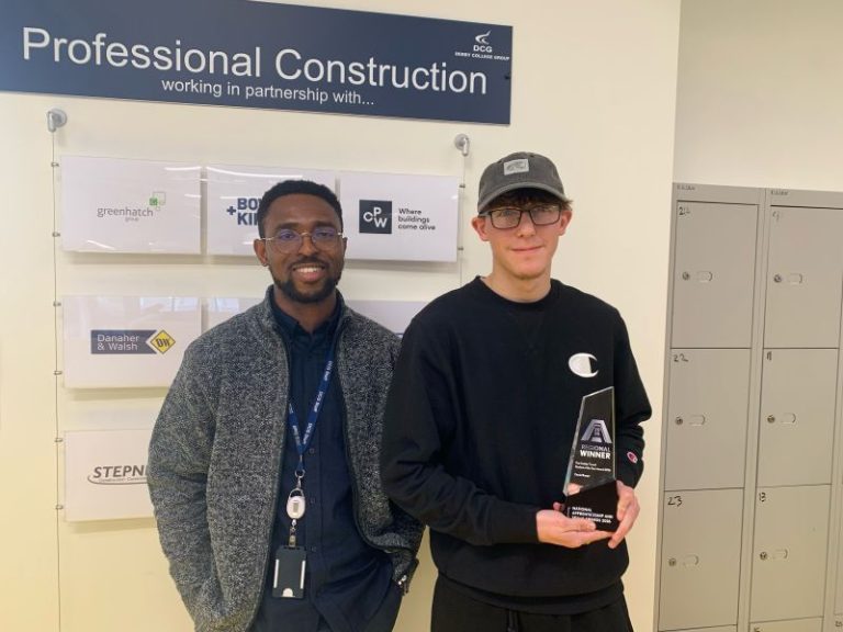 Teacher of CAD and BIM at Derby College, Eugene Gbenedio, wearing a blue shirt and grey jumper stood next to Derby College apprentice Daniel Burgin, holding his award