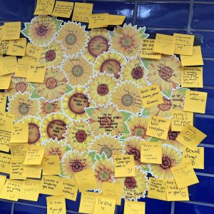 yellow notes with positive messages for World Mental Health Day stuck on a blue tiled wall.
