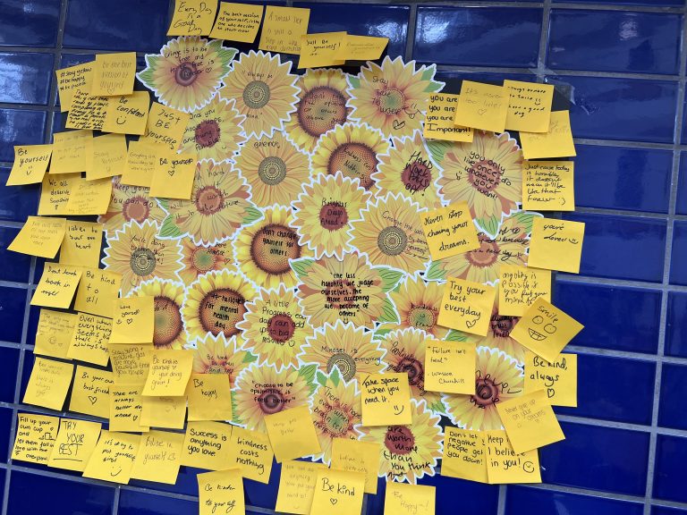 yellow notes with positive messages for World Mental Health Day stuck on a blue tiled wall.